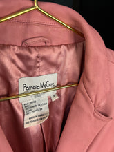 Load image into Gallery viewer, Close-up of a pink leather jacket hanging on a gold hanger, showing the interior collar and a visible Pamela McCox brand label.
